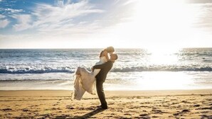 Un couple s’embrasse sur une plage, avec l’océan en arrière-plan.