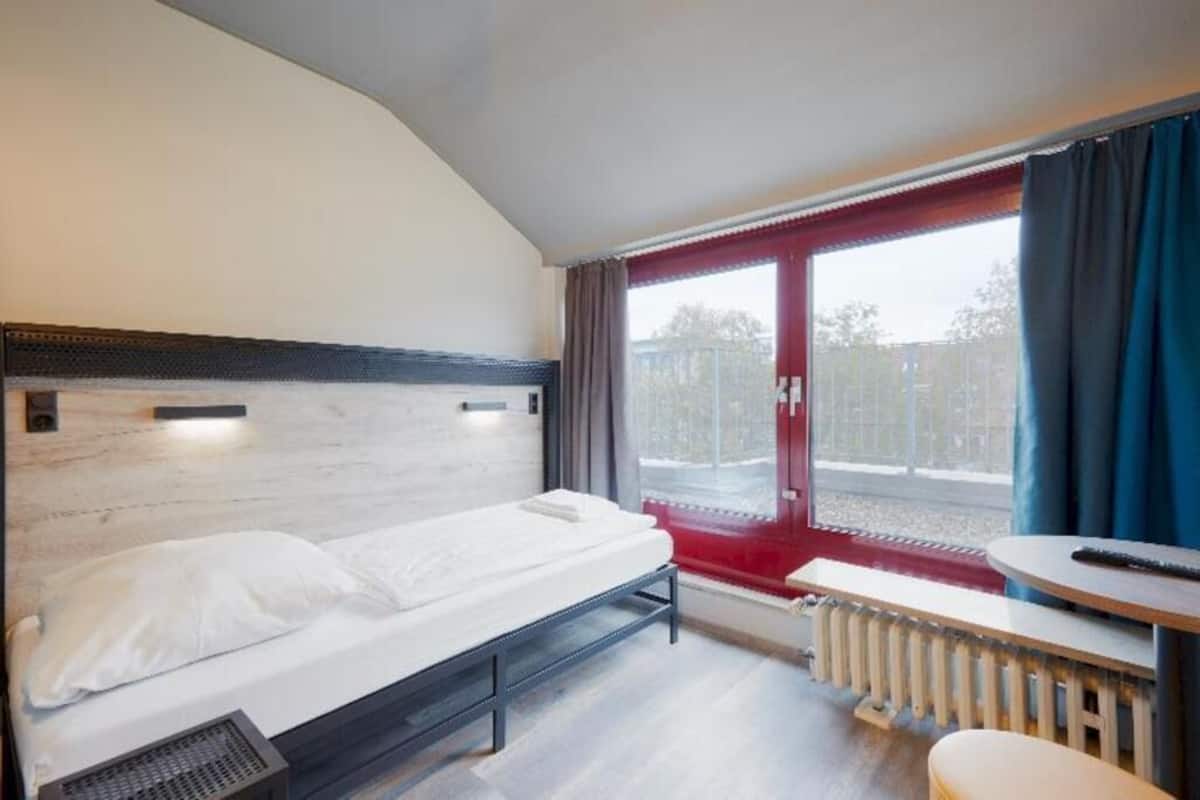 Habitación de hotel con cama, una mesita, un banco y una ventana con cortinas.