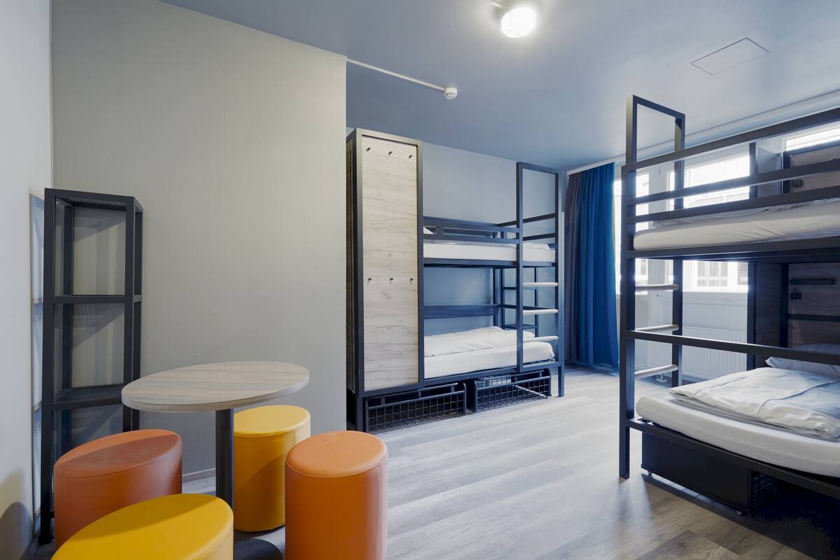 Una habitación moderna y compacta con literas, una pequeña mesa redonda y dos taburetes naranjas.