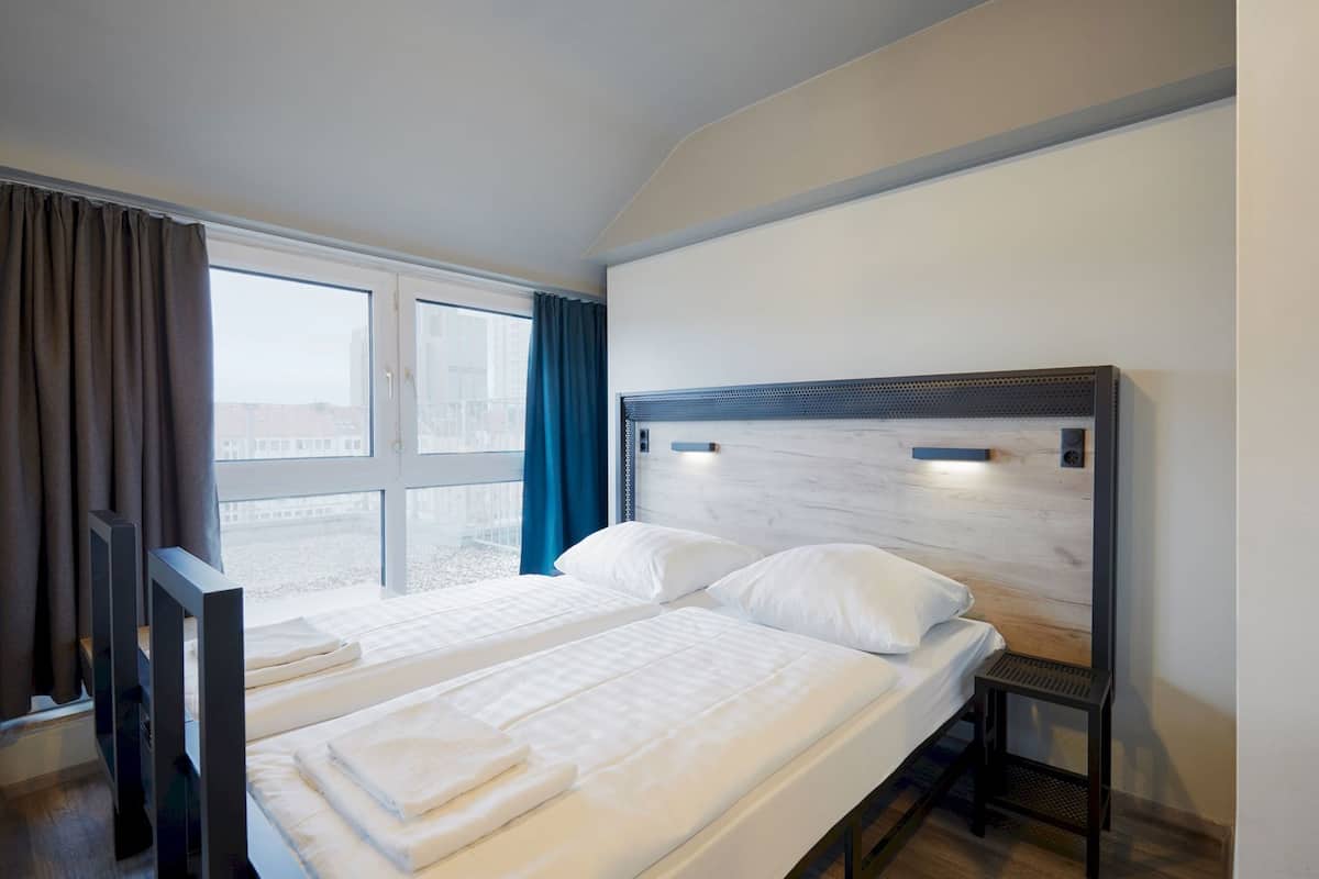 Una habitación de hotel con cama, ventana, cortinas y cabecero.