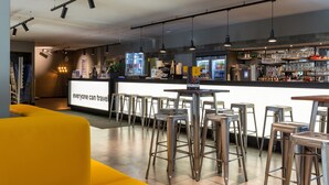 A modern bar area with metal stools, a counter, and a neon sign. - a&o Düsseldorf Hauptbahnhof (Düsseldorf)
