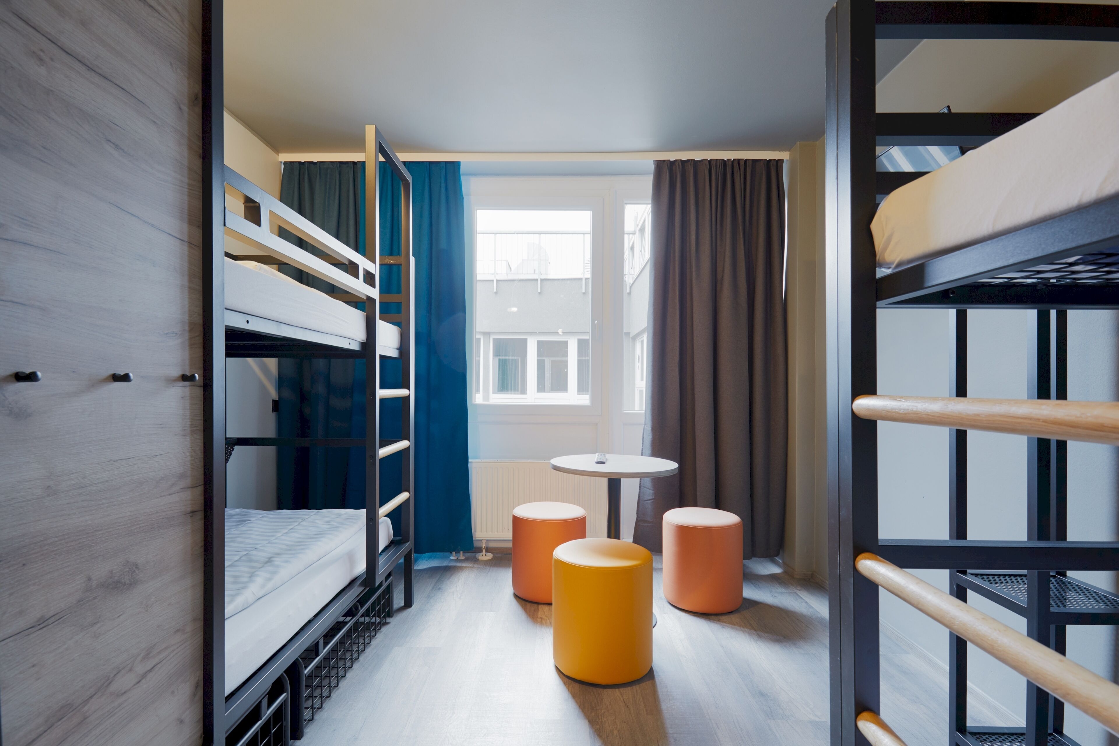 A compact room with bunk beds, a small round table, and two stools.