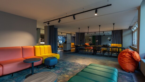 A modern living area with a sofa, chairs, and a coffee table. There is a dining area in the background with a table and chairs. - a&o Düsseldorf Hauptbahnhof (Düsseldorf)