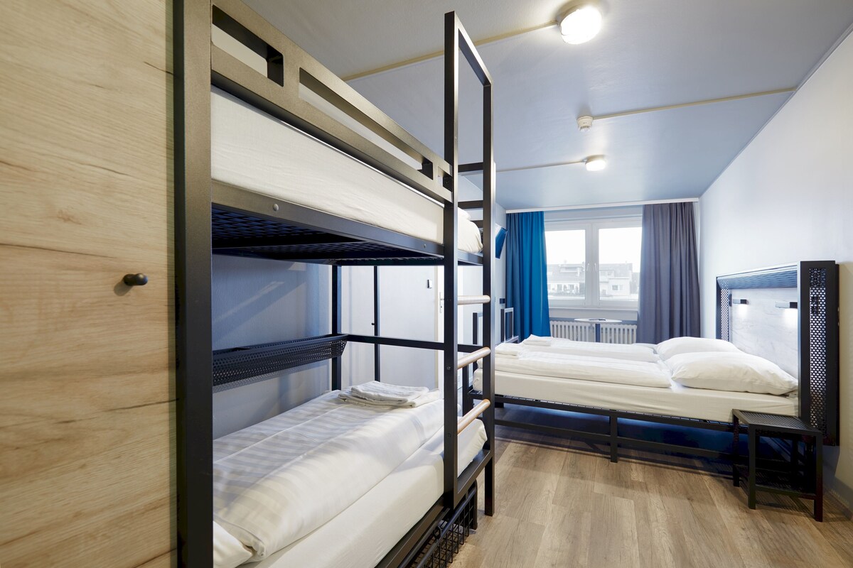 Una habitación con literas, una puerta de madera y una ventana con cortinas.