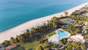 An aerial view of a coastal resort with a sandy beach, a swimming pool, and a tennis court. - VOI Floriana Resort (Simeri-Crichi)