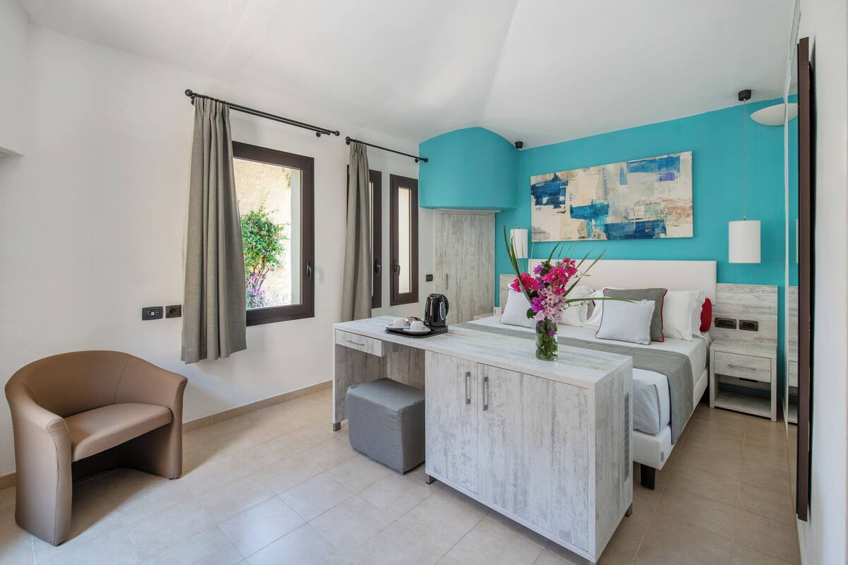 A modern bedroom with a bed, bedside tables, a desk, a chair, and a window with curtains.