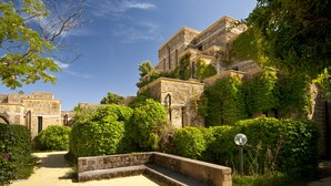 A courtyard with stone benches, a pathway, and lush greenery. - VOI Floriana Resort (Simeri-Crichi)
