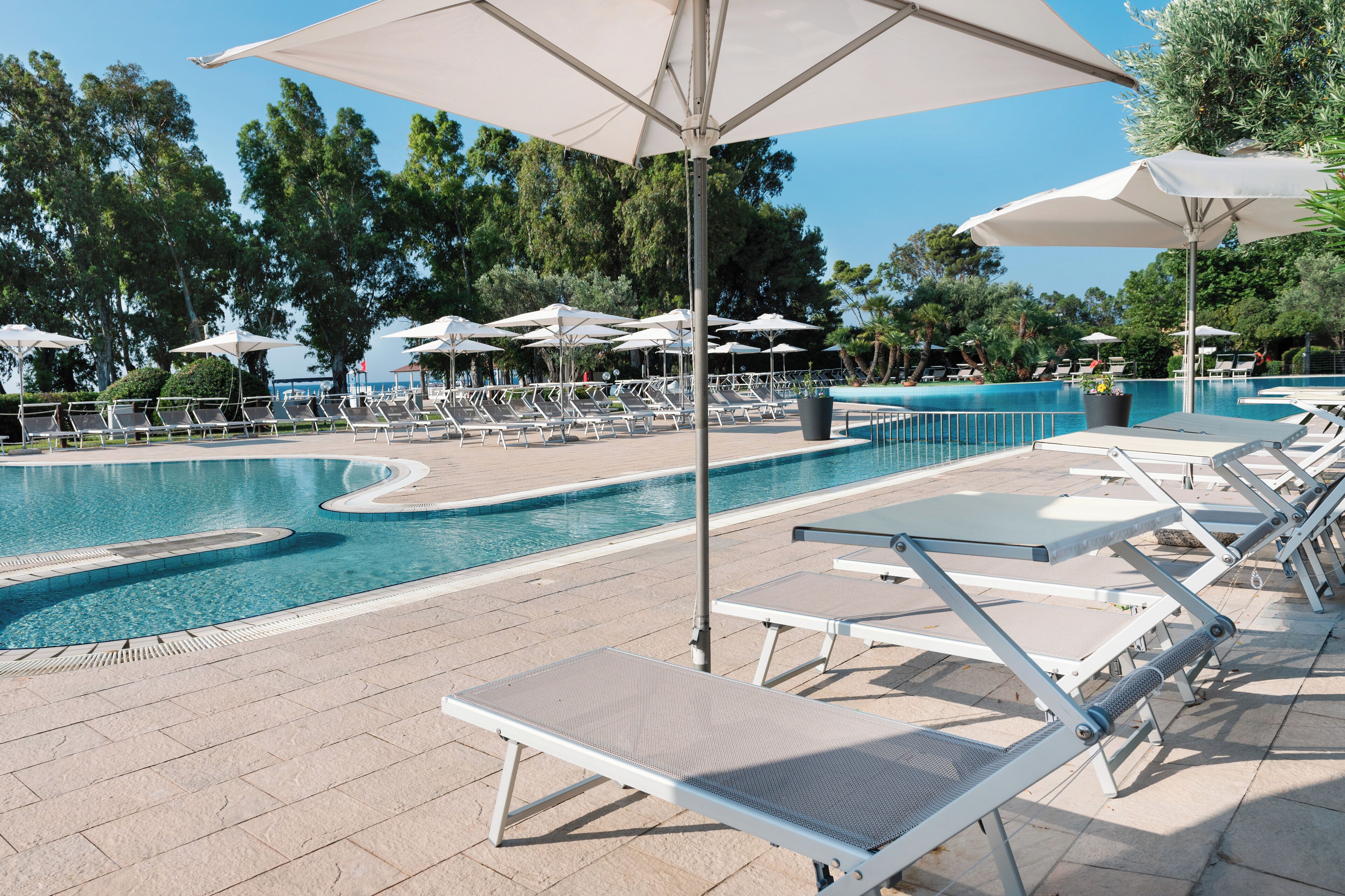 A poolside area with sun loungers and umbrellas, surrounded by trees.