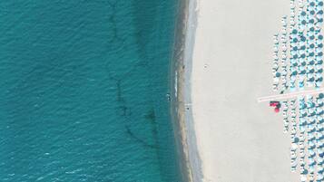 Vista aérea de uma praia com fileiras de guarda-sóis e cadeiras de praia, uma costa arenosa e um mar azul cristalino.