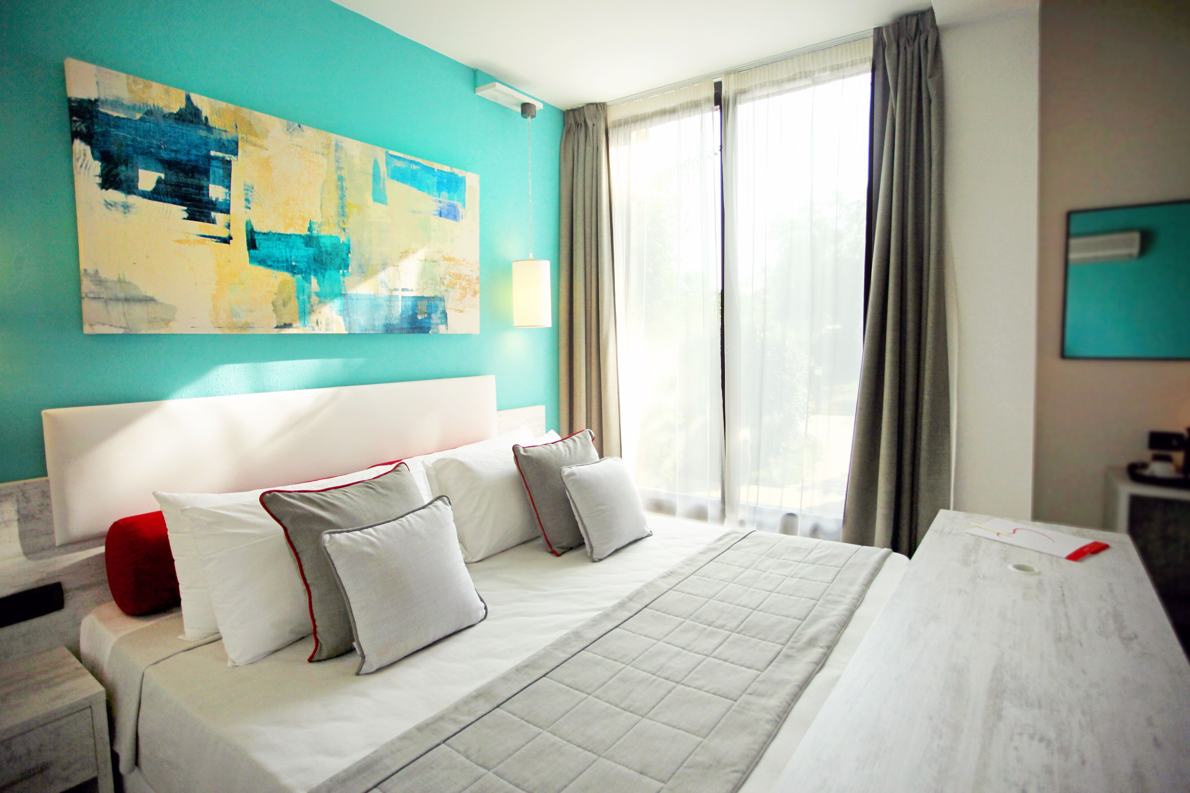 A hotel room with a large bed, a headboard, a painting on the wall, and a window with curtains.