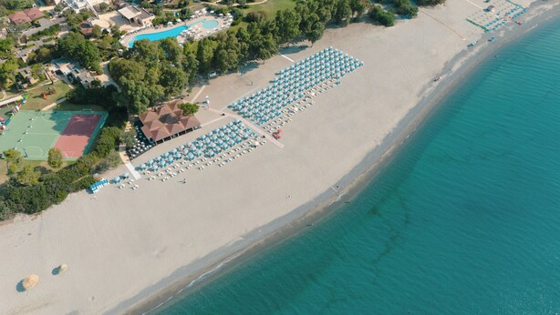 An aerial view of a beach with rows of umbrellas and lounge chairs, a pool, and a tennis court. - VOI Floriana Resort (Simeri-Crichi)