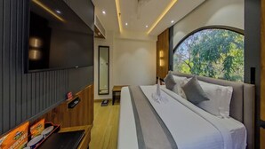 A modern hotel room with a large bed, a flat-screen TV, a ceiling fan, and a window with a view of trees. - Lords Inn Vadodara (Vadodara)