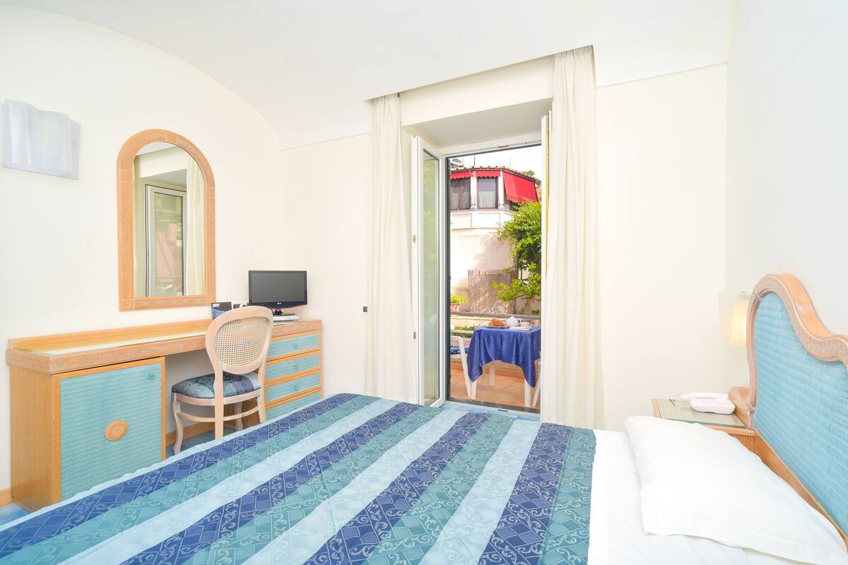 A hotel room with a bed, a desk, a chair, a television, and a view of the outside.