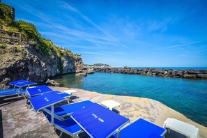 A beachside hotel with blue sun loungers and a rocky cliff. - Albergo Terme Italia (Casamicciola Terme)