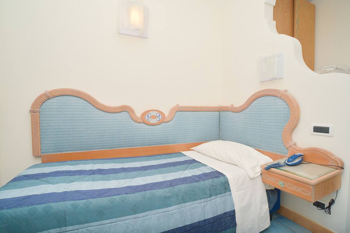 A bed with a striped bedspread, a bedside table with a phone, and a wall-mounted light fixture.