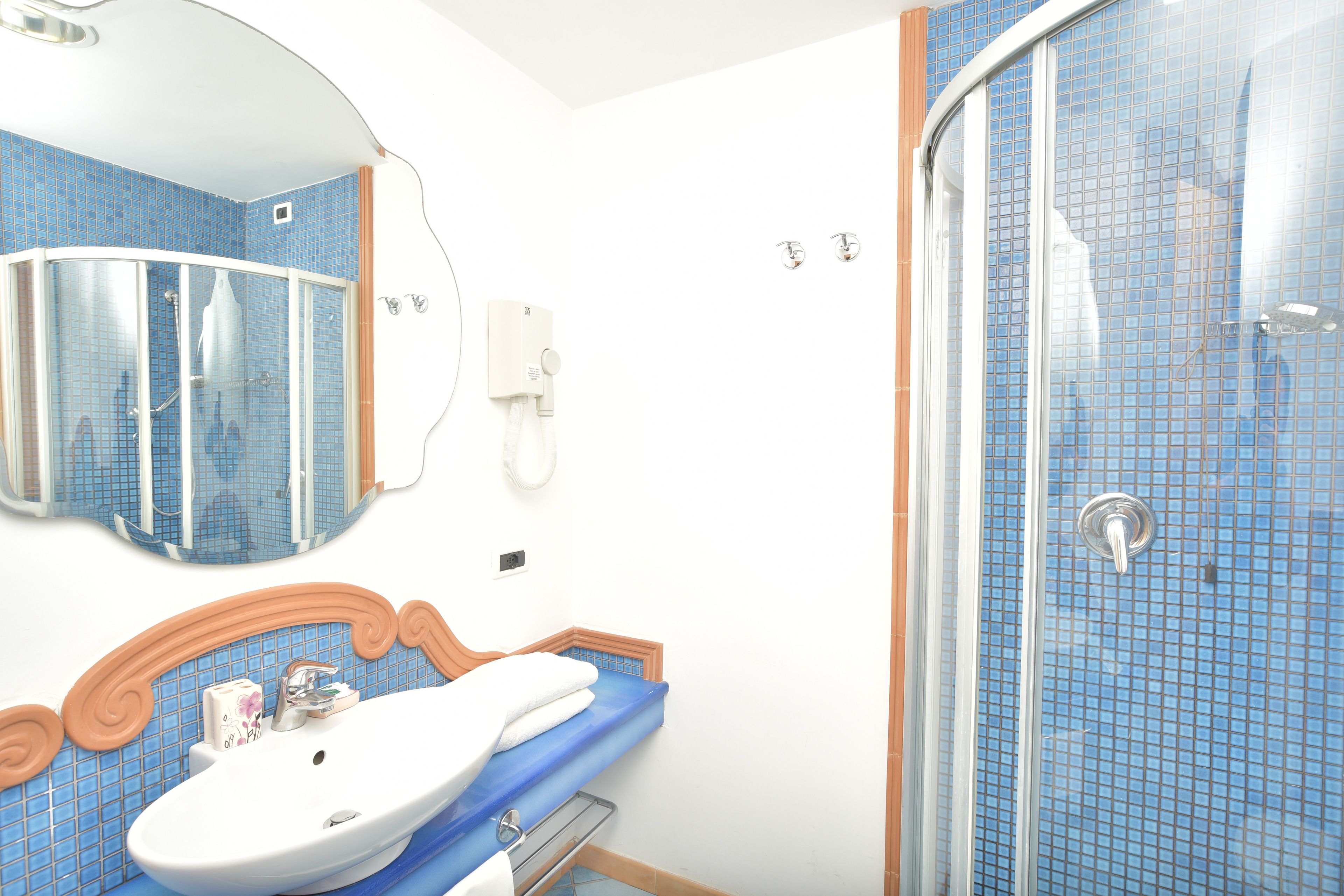 Une salle de bain avec une cabine de douche aux parois incurvées, un lavabo avec un miroir au-dessus et un téléphone fixé au mur.