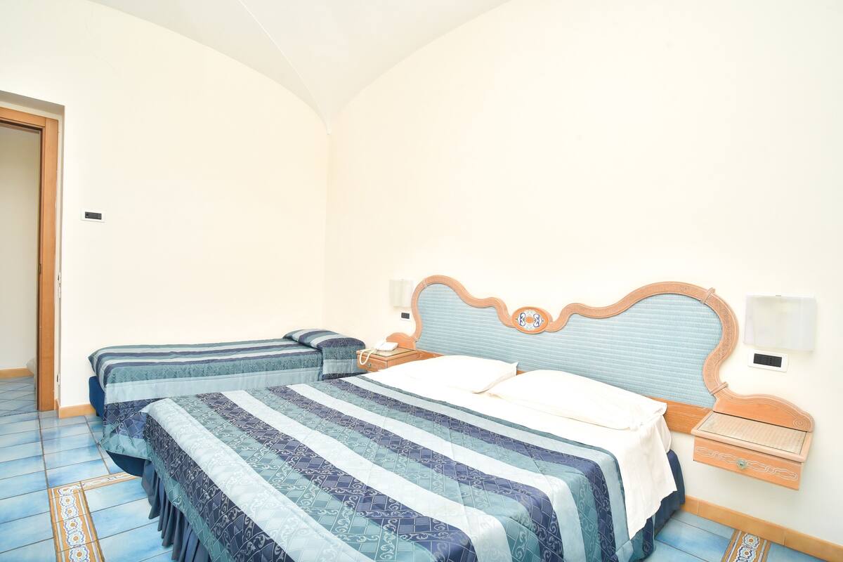 A hotel room with two beds, a wooden headboard, a nightstand, and a wall-mounted light fixture.