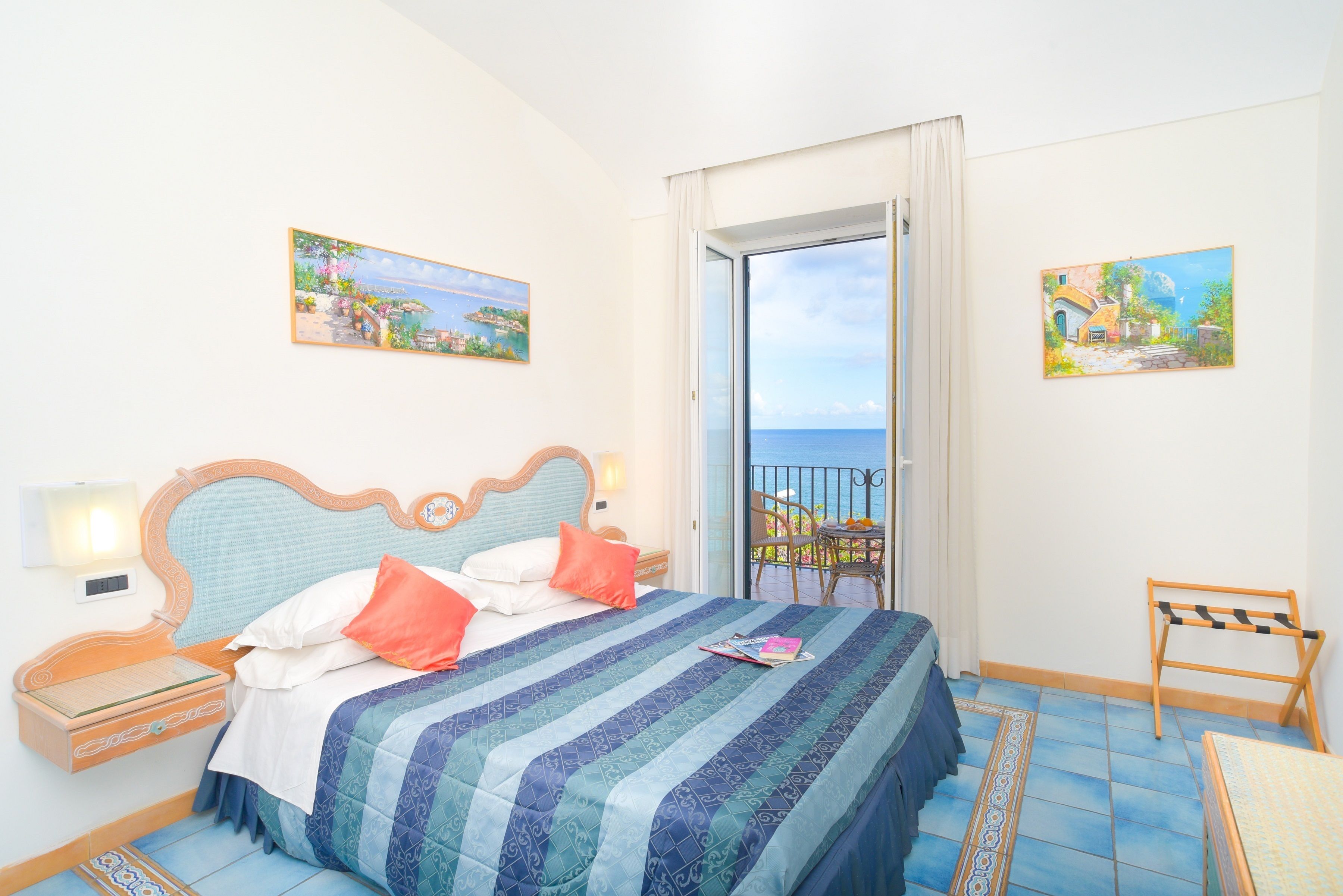 Een slaapkamer met een bed, nachtkastjes, een stoel en uitzicht op zee.