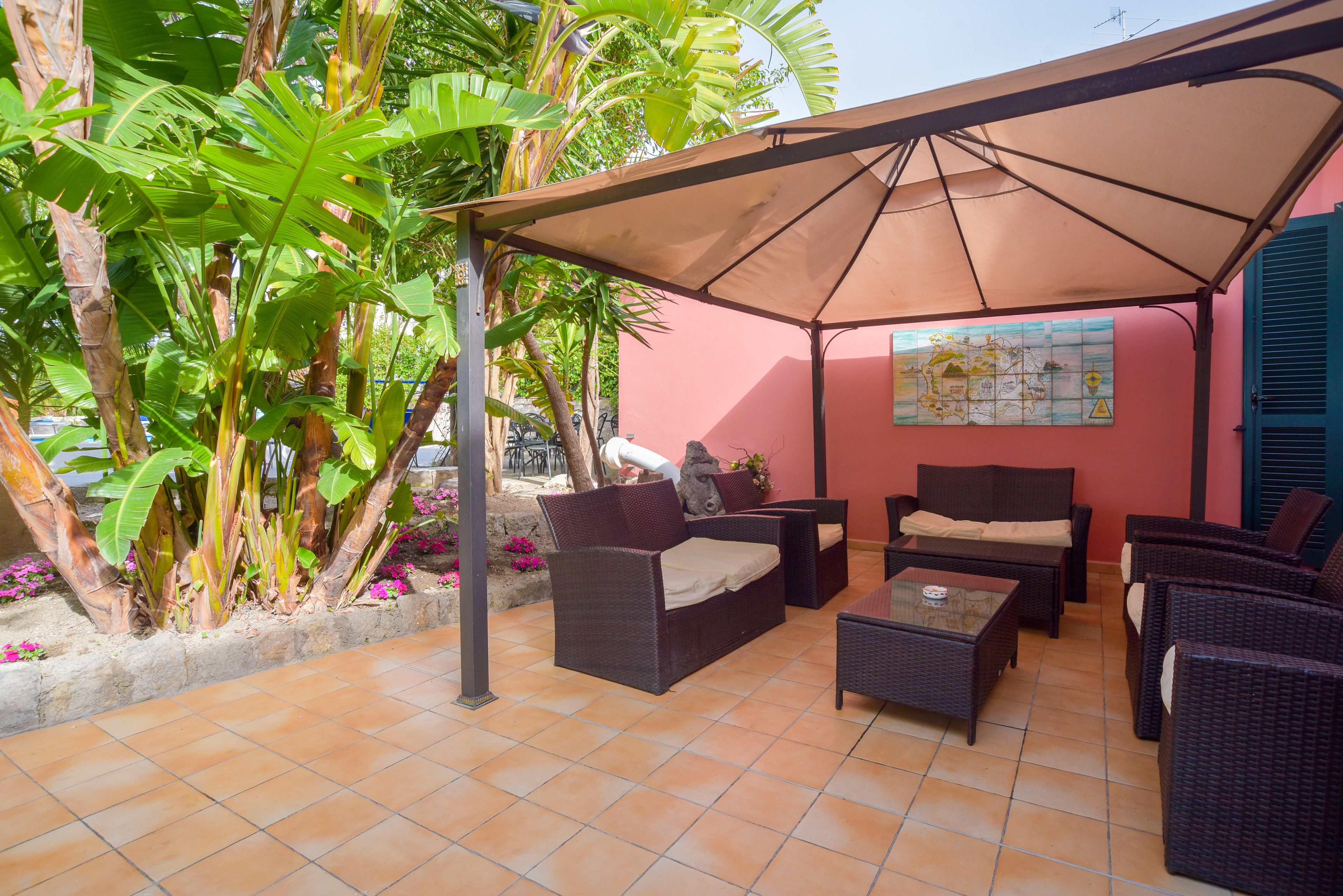 Eine Terrasse im Freien mit Korbmöbeln, einer Karte an der Wand und tropischen Pflanzen.