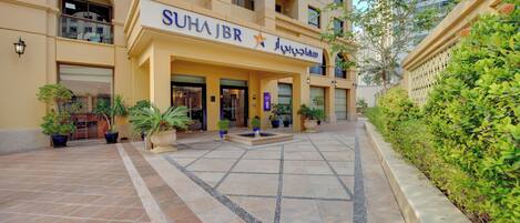 A hotel entrance with a tiled courtyard, potted plants, and a sign reading "SUHAJBR".