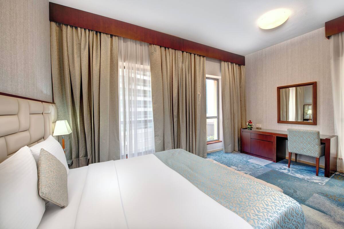 Een hotelkamer met een groot bed, een bureau, een stoel, een spiegel en een raam met gordijnen.