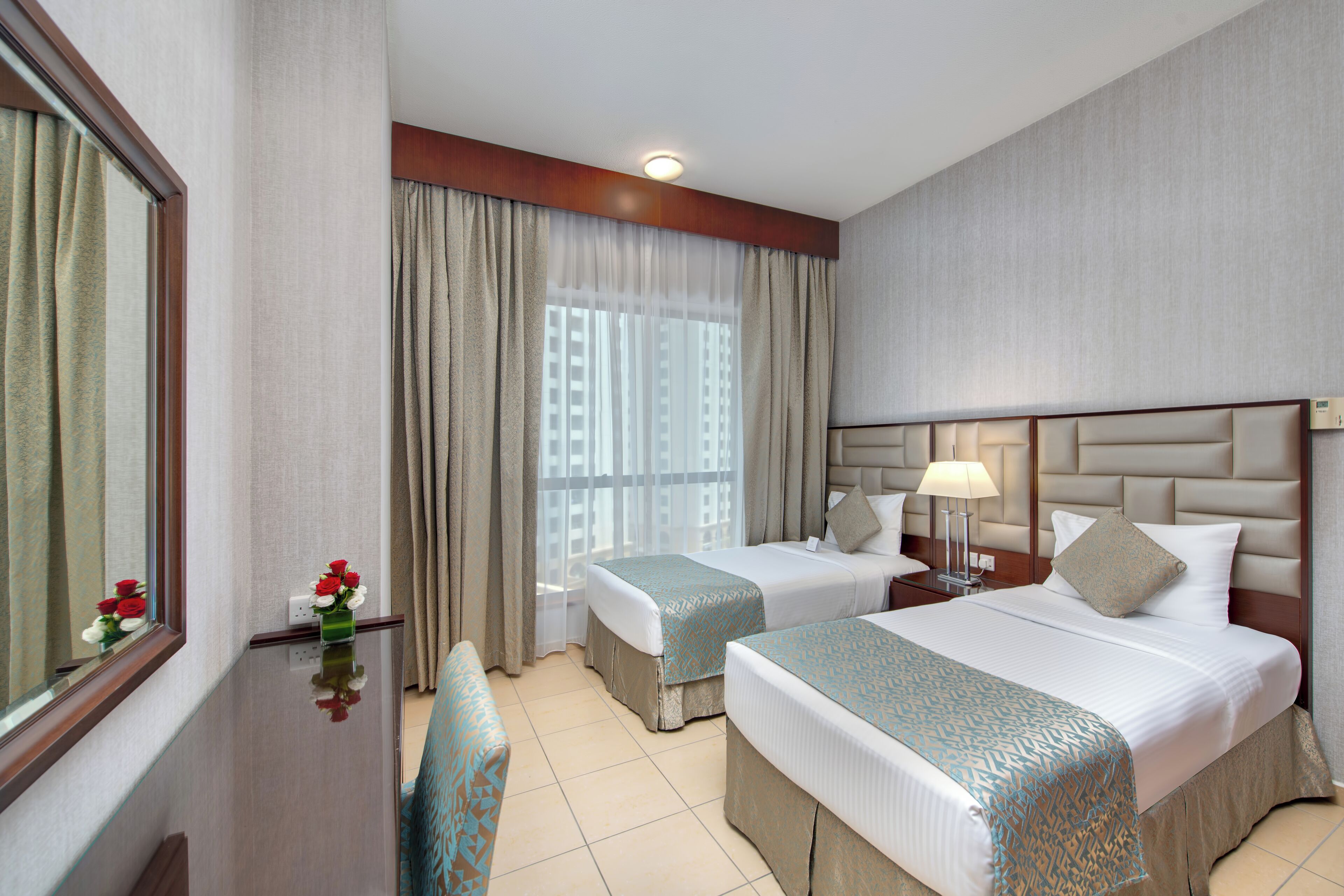 A hotel room with two beds, a nightstand, a mirror, and a window with curtains.
