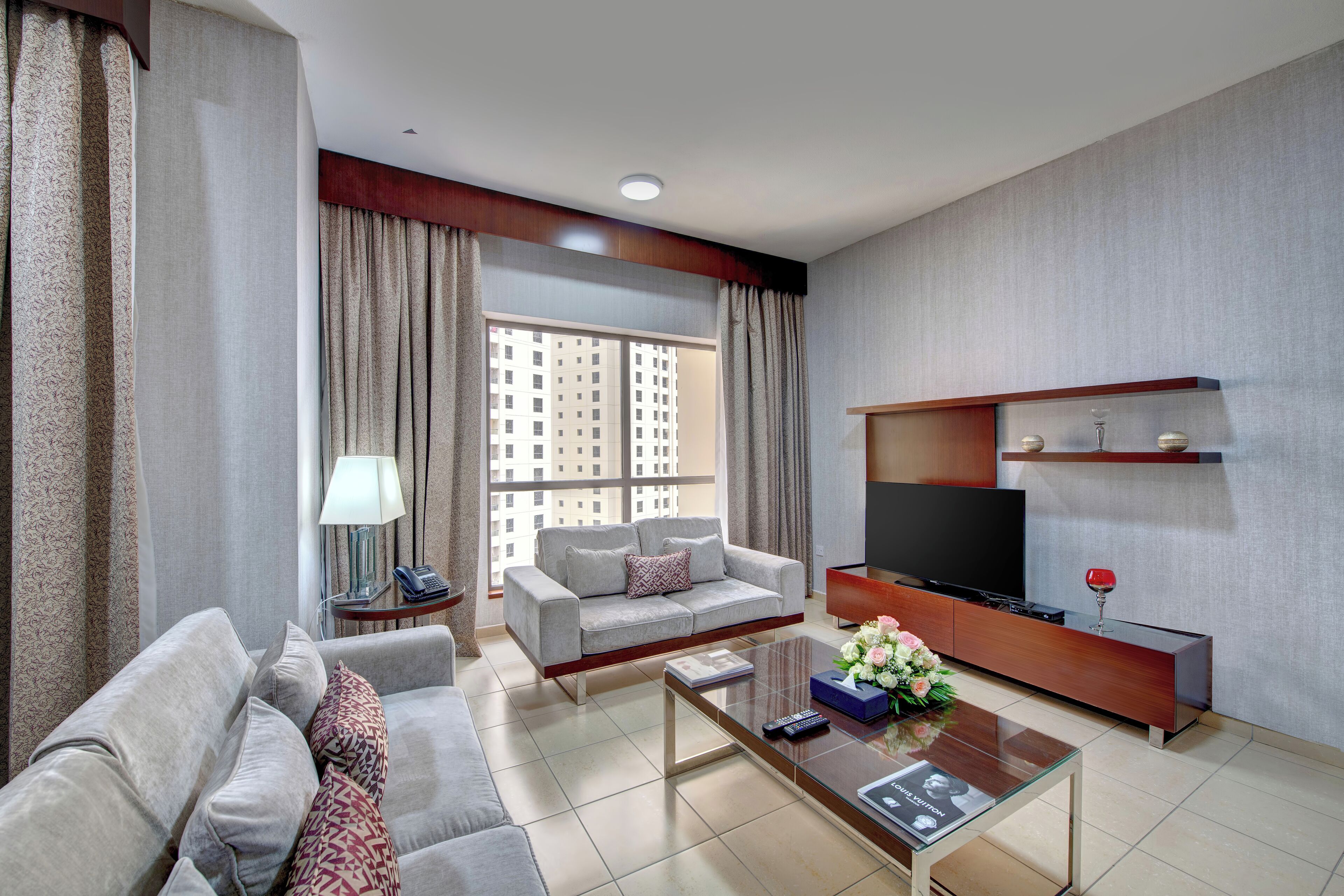 Una sala de estar moderna con sofá, sillón, mesa de centro, televisor y vistas al balcón.