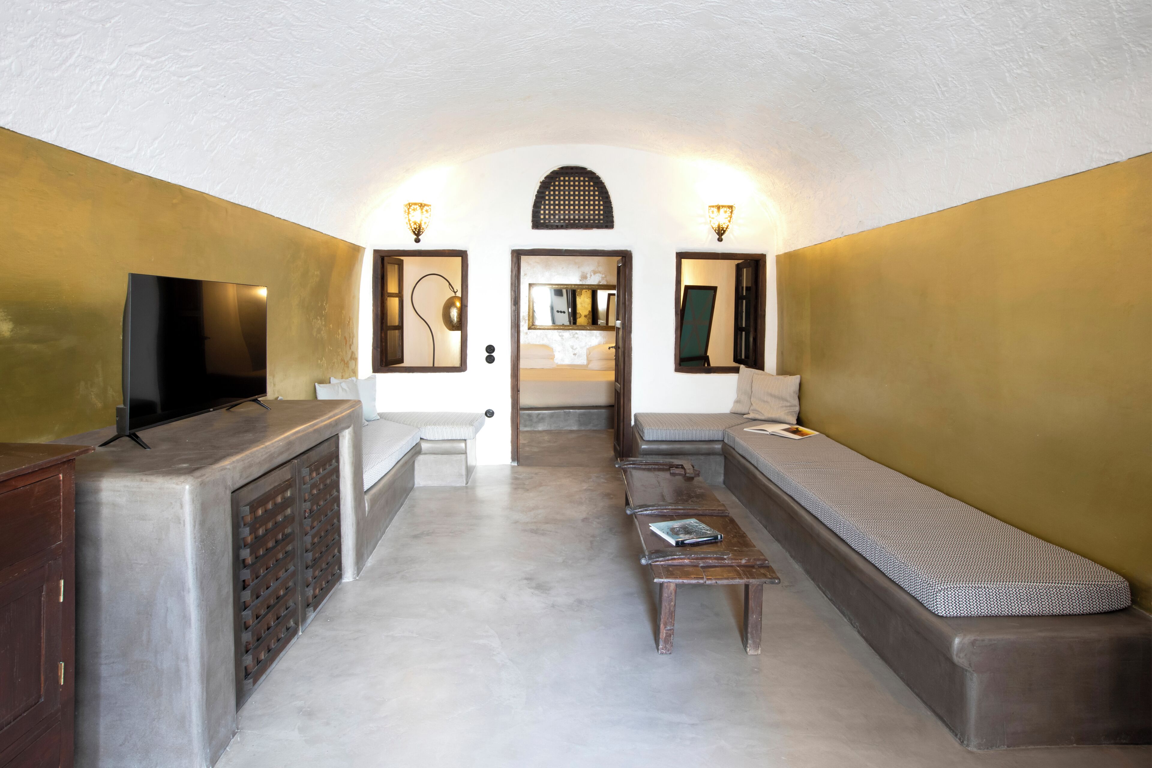 A compact hotel room with a sofa, a small table, a TV, and a mirror.