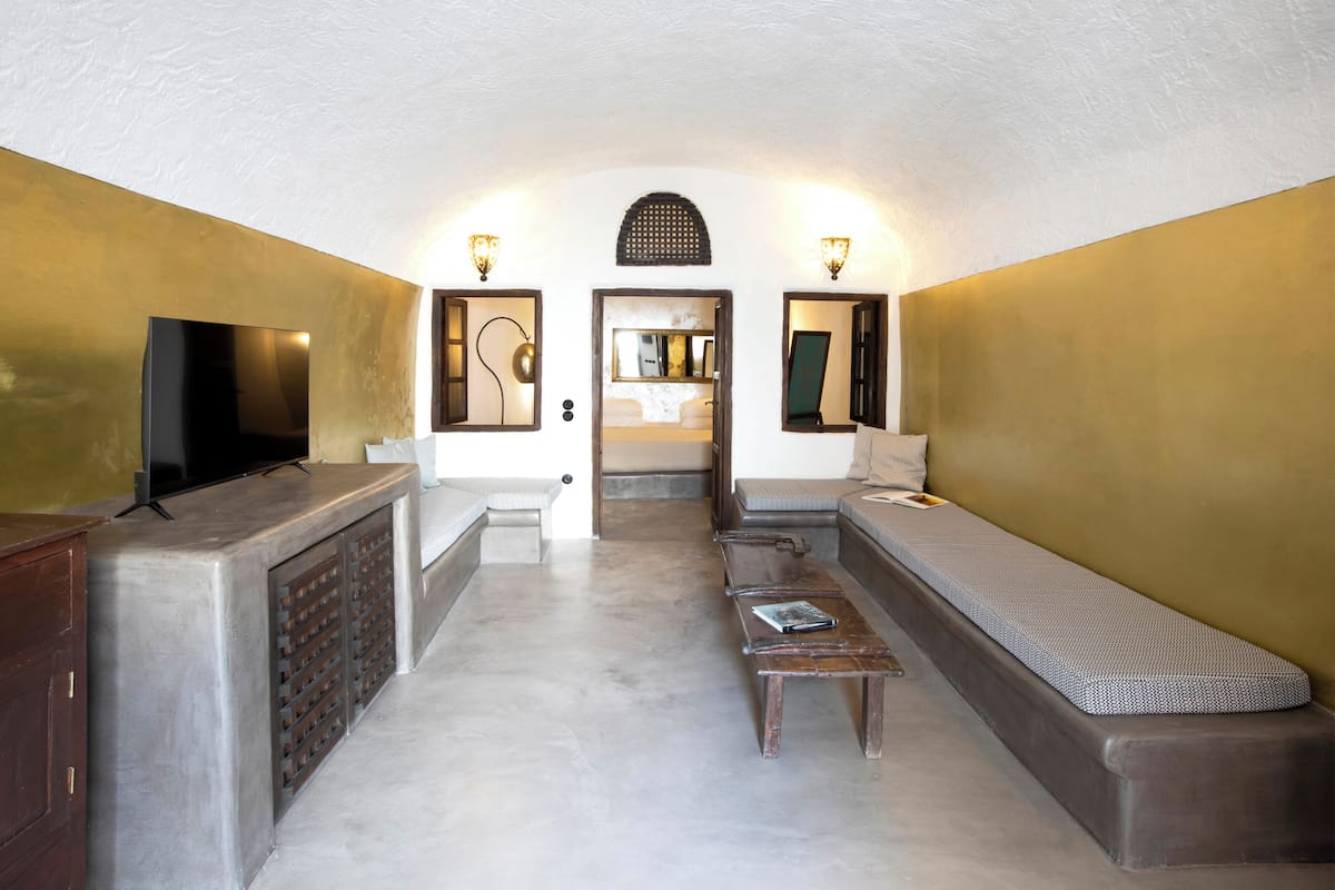 A compact hotel room with a sofa, a small table, a TV, and a mirror.