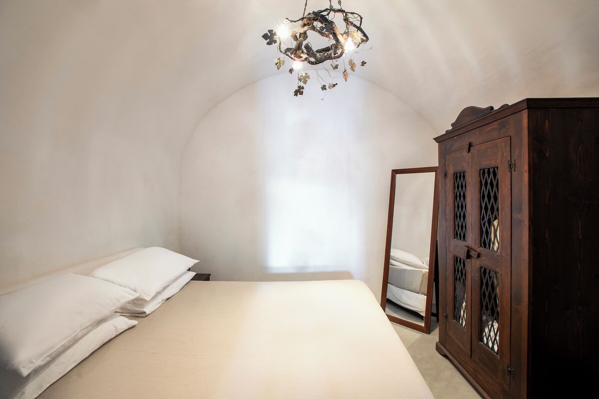 A bedroom with a bed, a wooden wardrobe, and a chandelier.