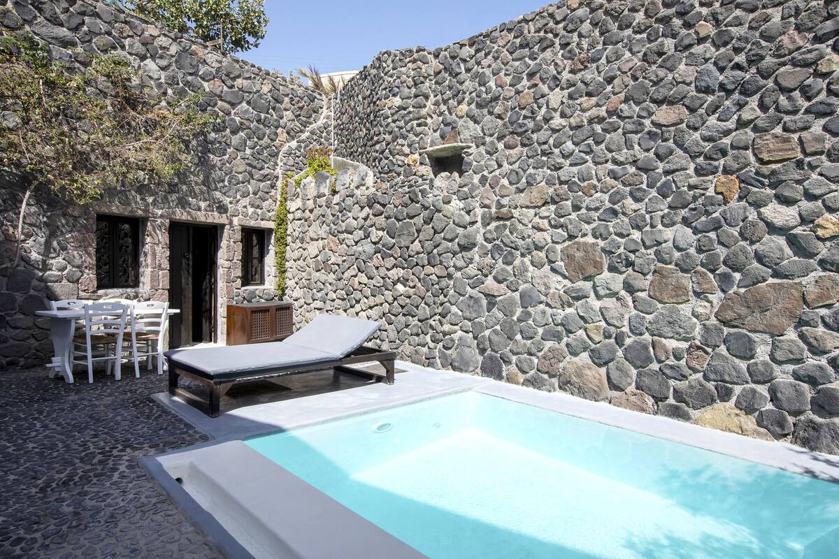 A stone-walled pool area with a lounge chair and a table with chairs.