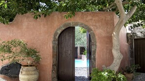 An arched doorway leading to a courtyard with a pool, surrounded by stone walls and potted plants. - Ducato Wine Village (Santorini)