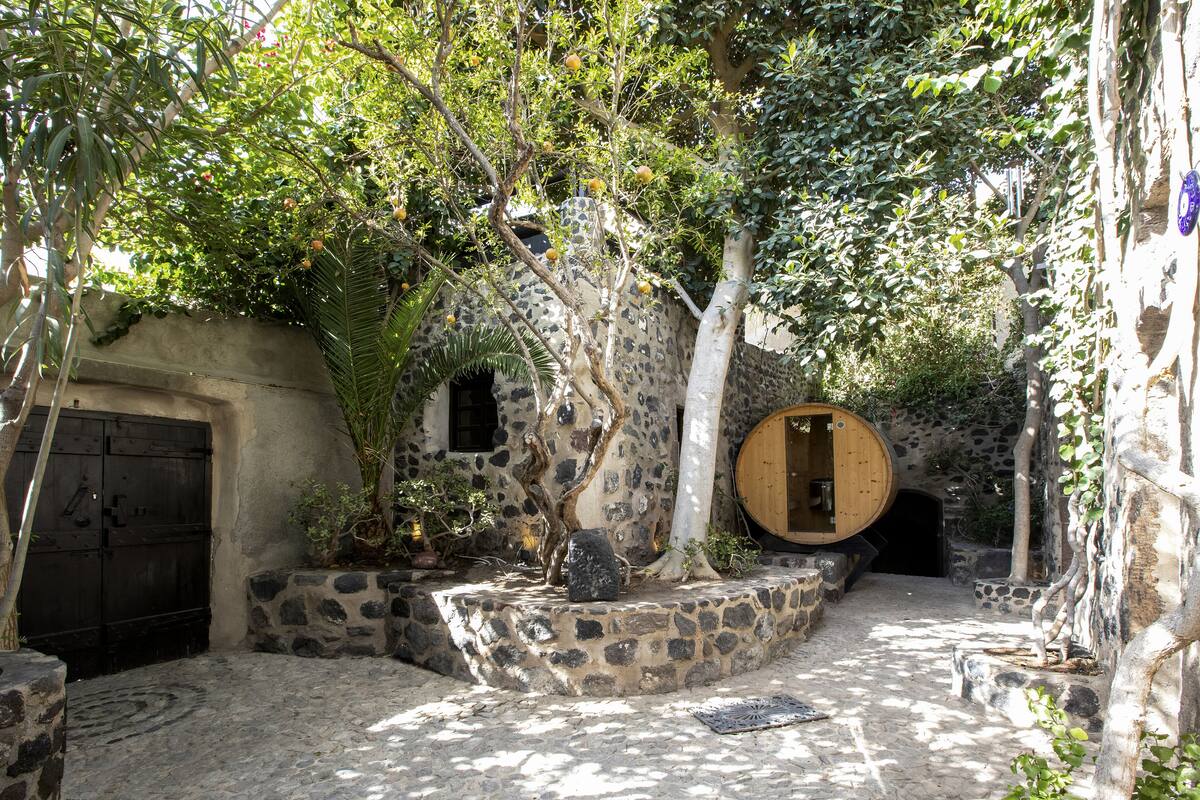 A rustic stone building with a wooden door and a round wooden barrel.