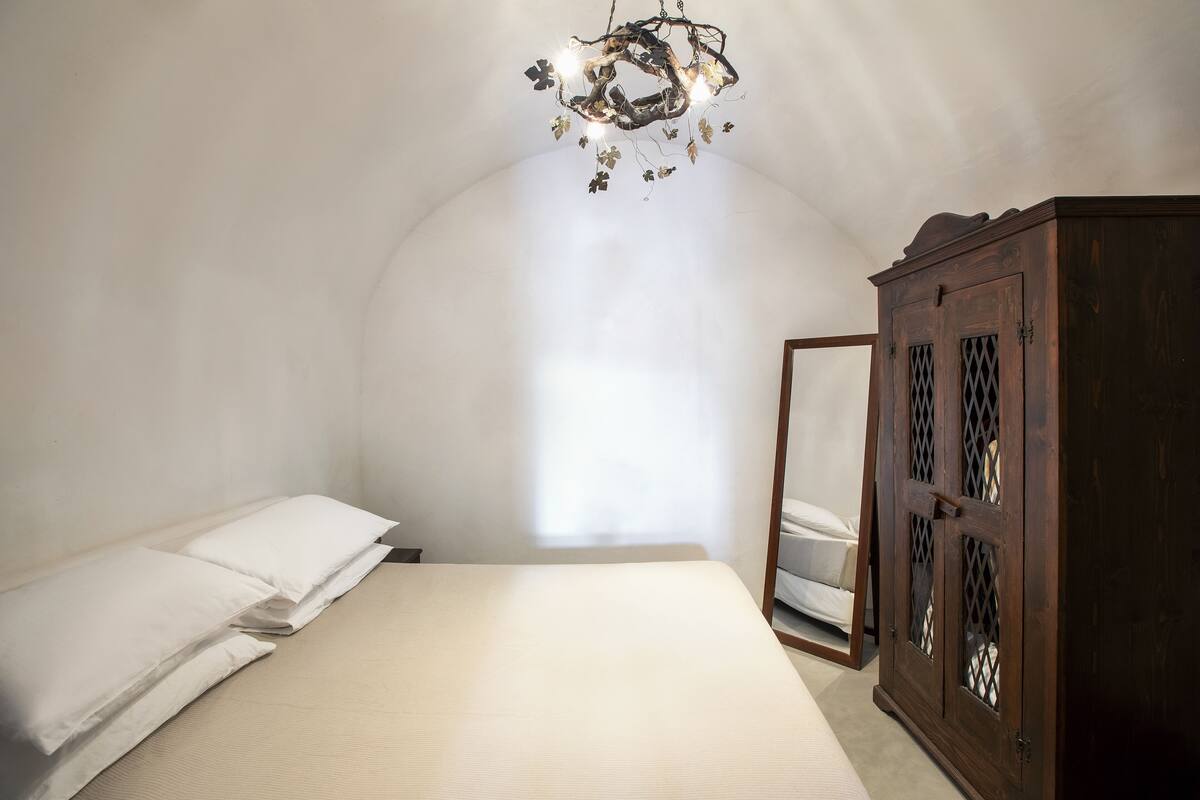 A bedroom with a bed, a wooden wardrobe, and a chandelier.