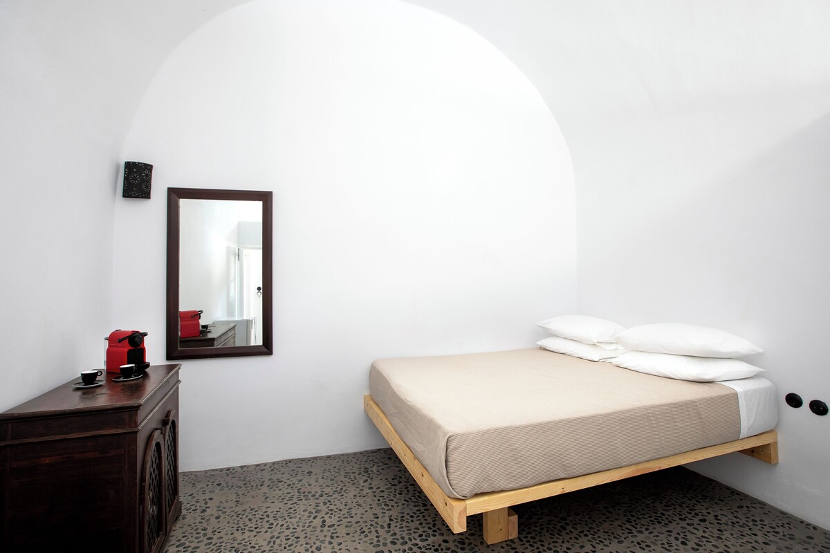 A minimalist bedroom with a bed, a dresser, a mirror, and a coffee maker.