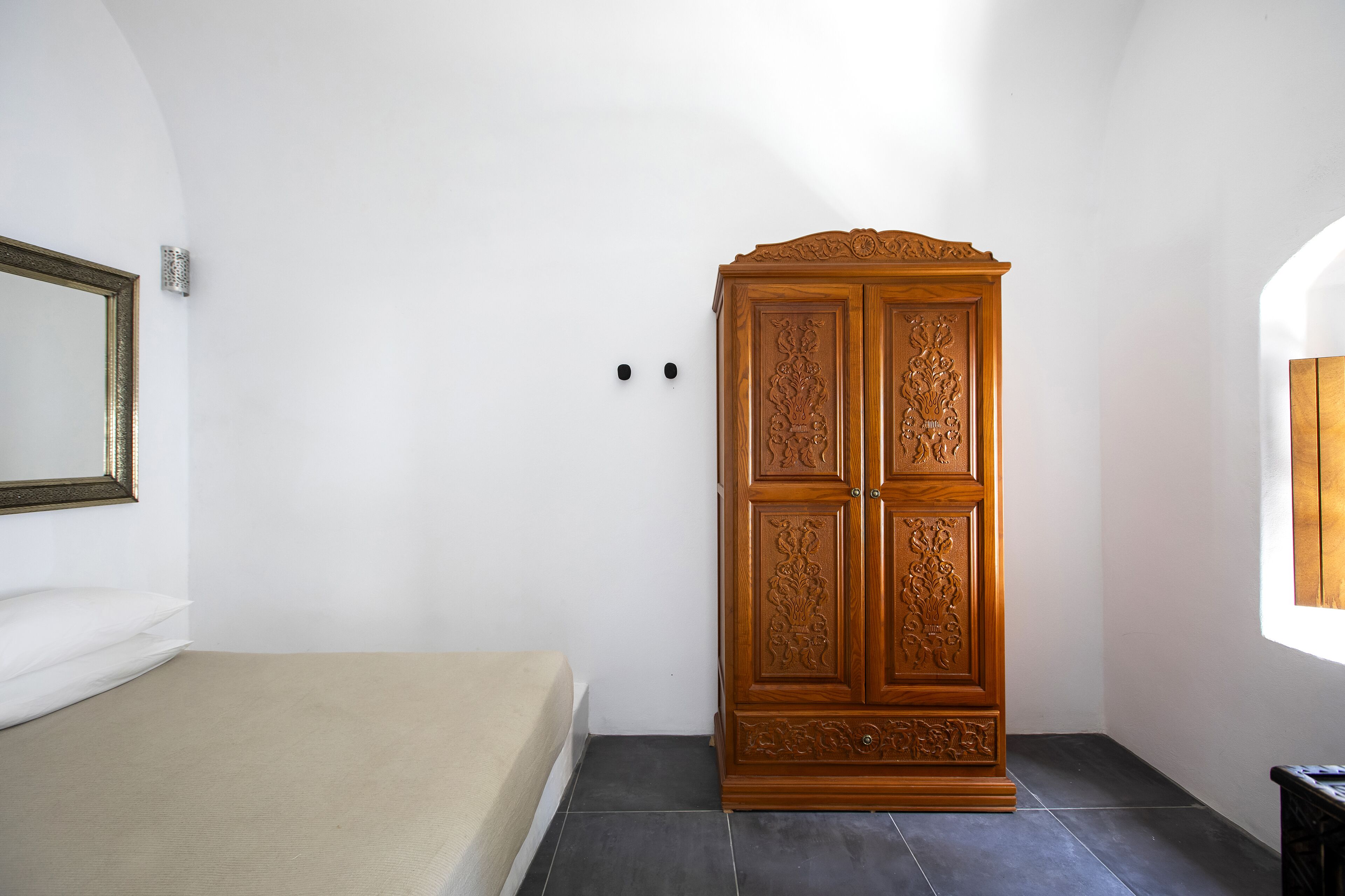 A bedroom with a bed, a wooden wardrobe, and a mirror on the wall.