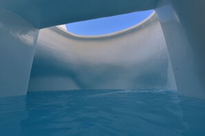 A view through a curved window into a water-filled space with a clear blue sky visible above.