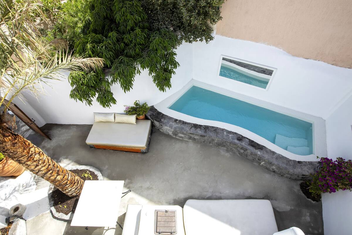 A rooftop pool area with a hot tub, lounge chairs, and surrounding greenery.