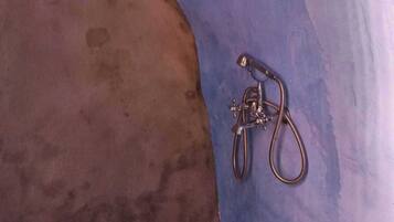 A bathroom with a blue and brown tiled wall, a shower head, and a hose.