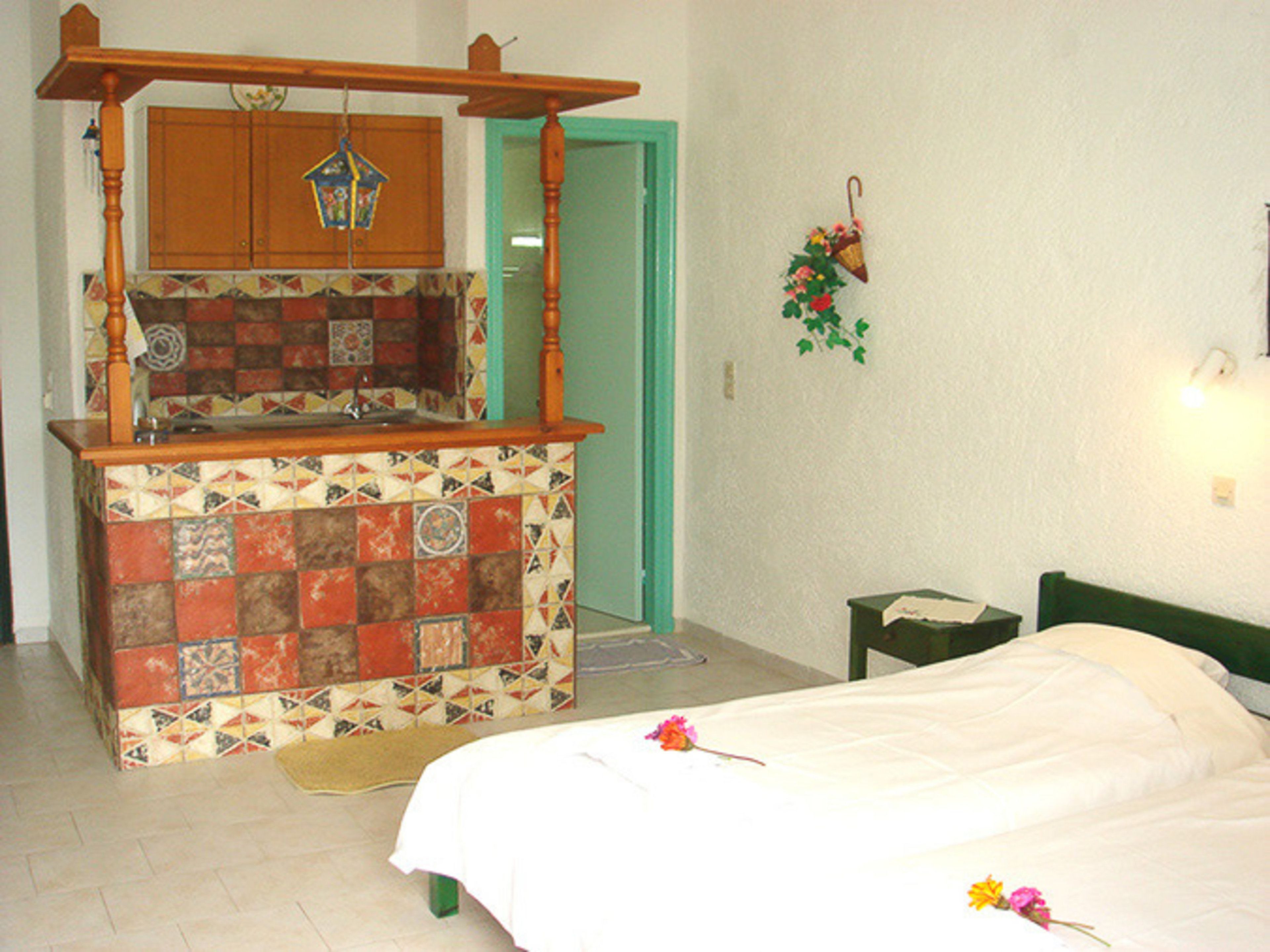 Une chambre à coucher comprenant un lit, une petite table de chevet, une commode, une fenêtre et une salle de bain avec un lavabo et un miroir.
