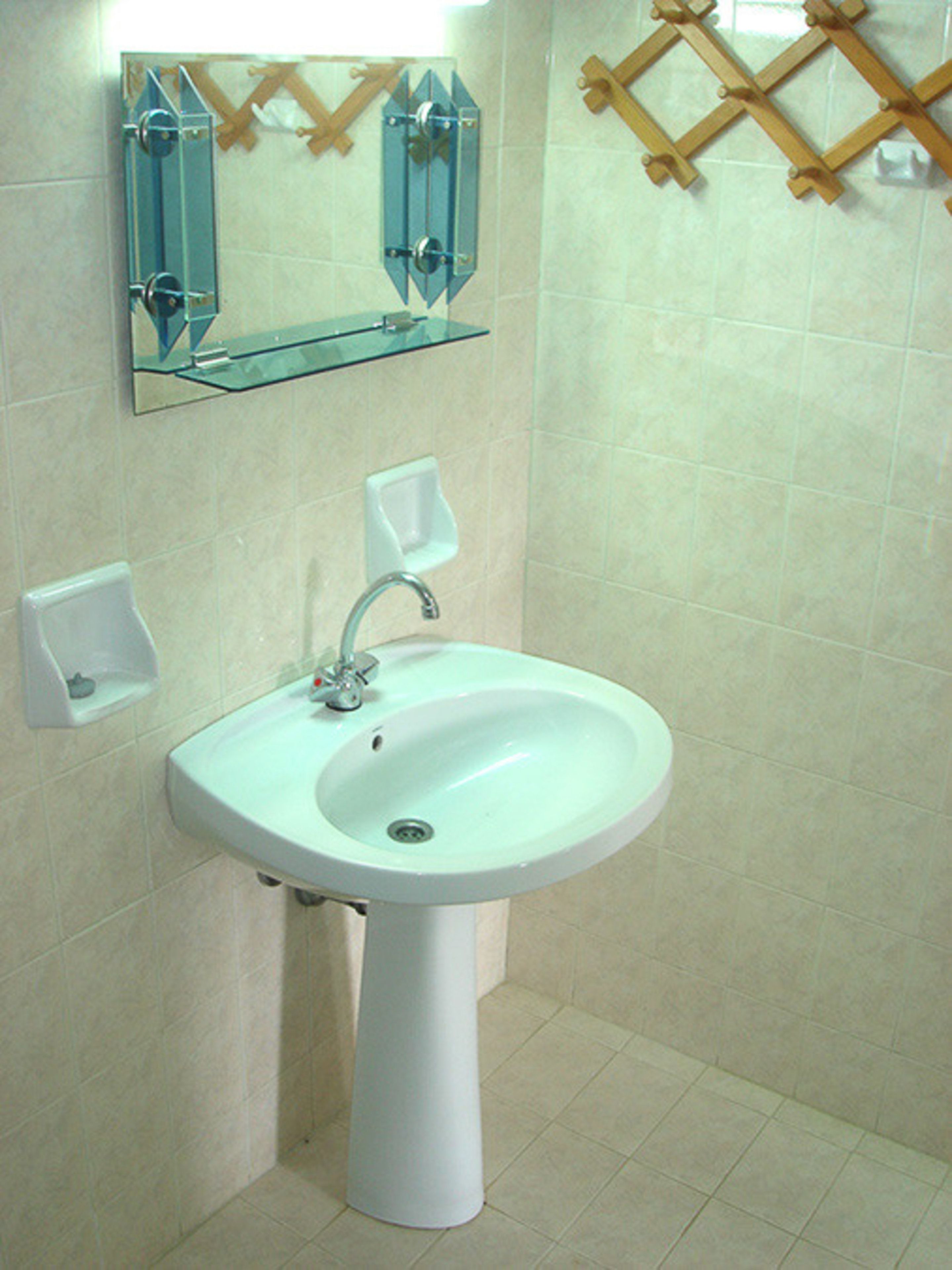 A bathroom with a white pedestal sink, a mirror above it, and a soap dispenser on the wall.