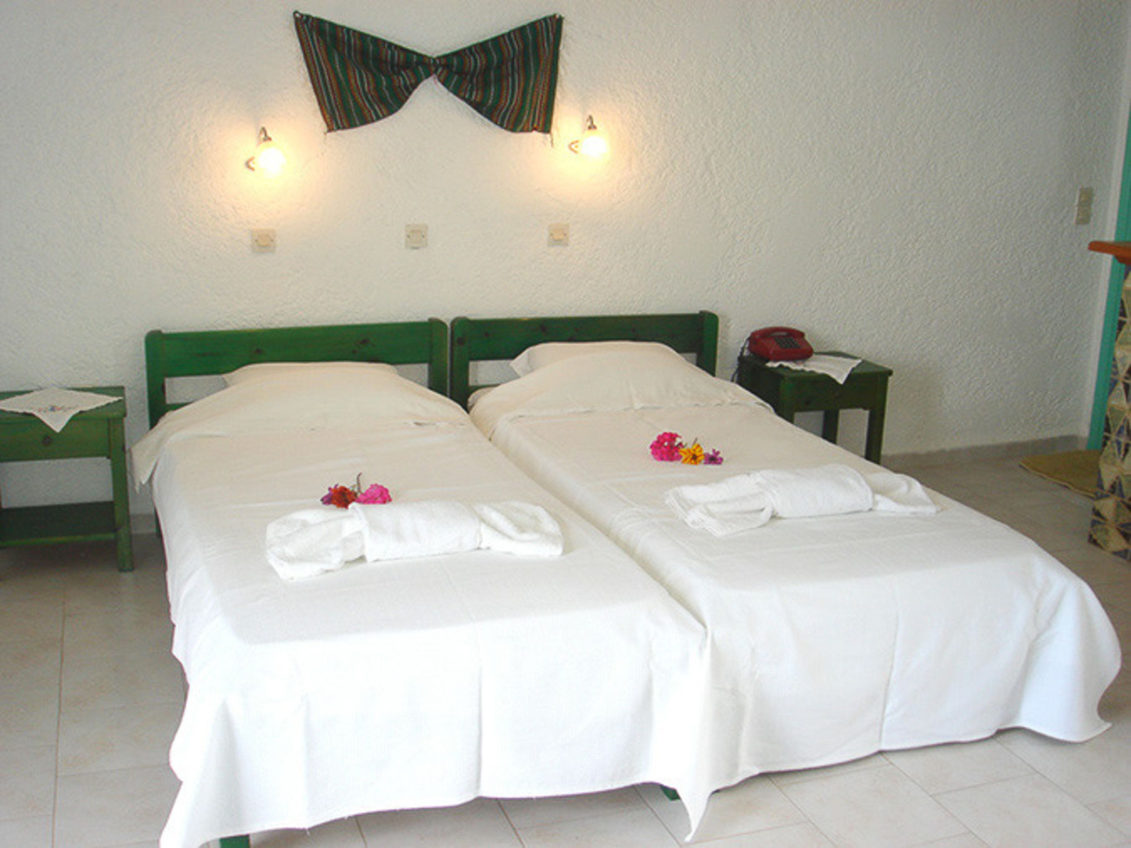 A double room with two beds, each with white linens and towels, a green headboard, a small bedside table with a lamp, and a telephone.