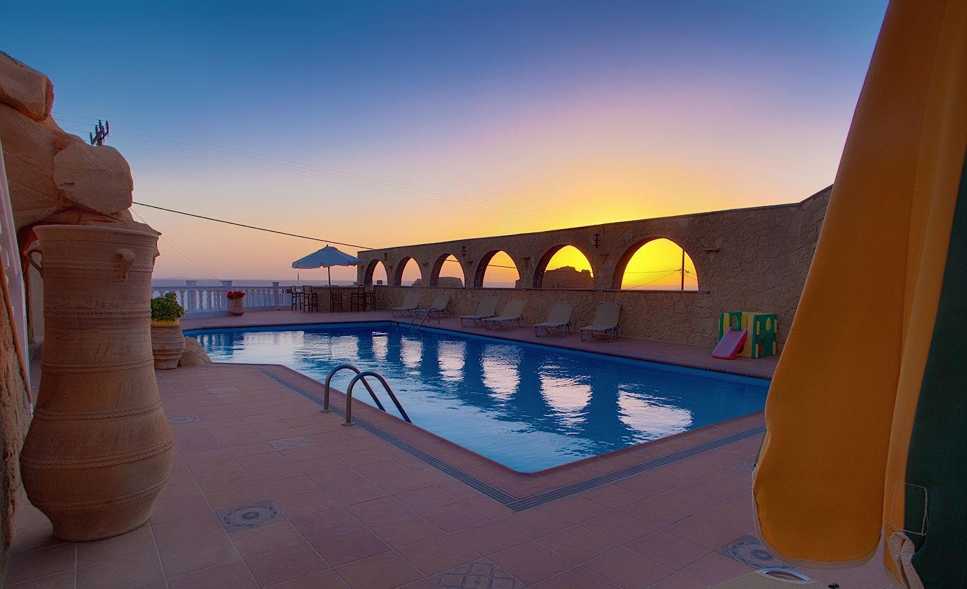 Un área de piscina con vista al atardecer, arcos de piedra y sillas de descanso.