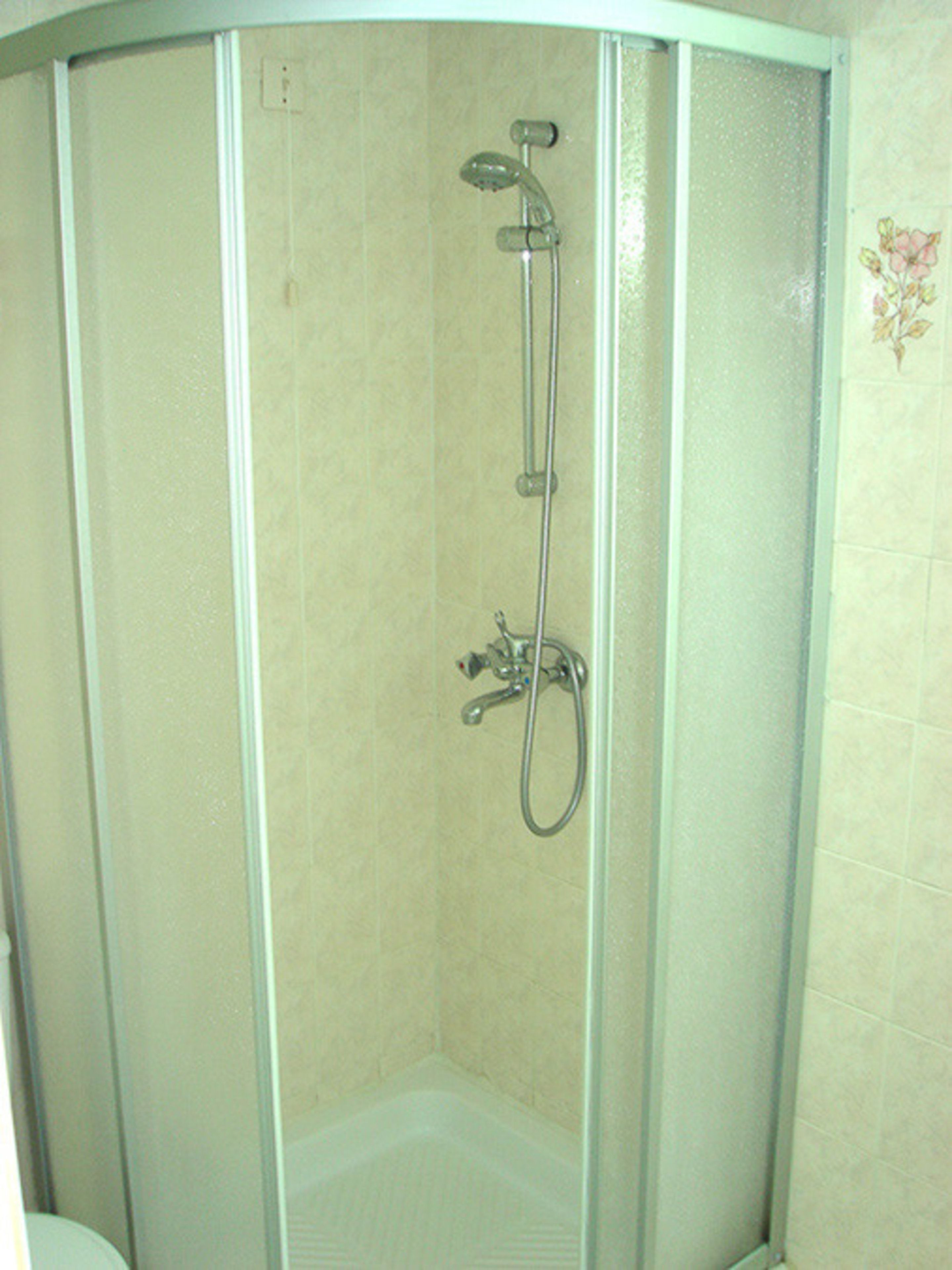A glass-enclosed shower stall with a handheld showerhead and a handheld faucet.