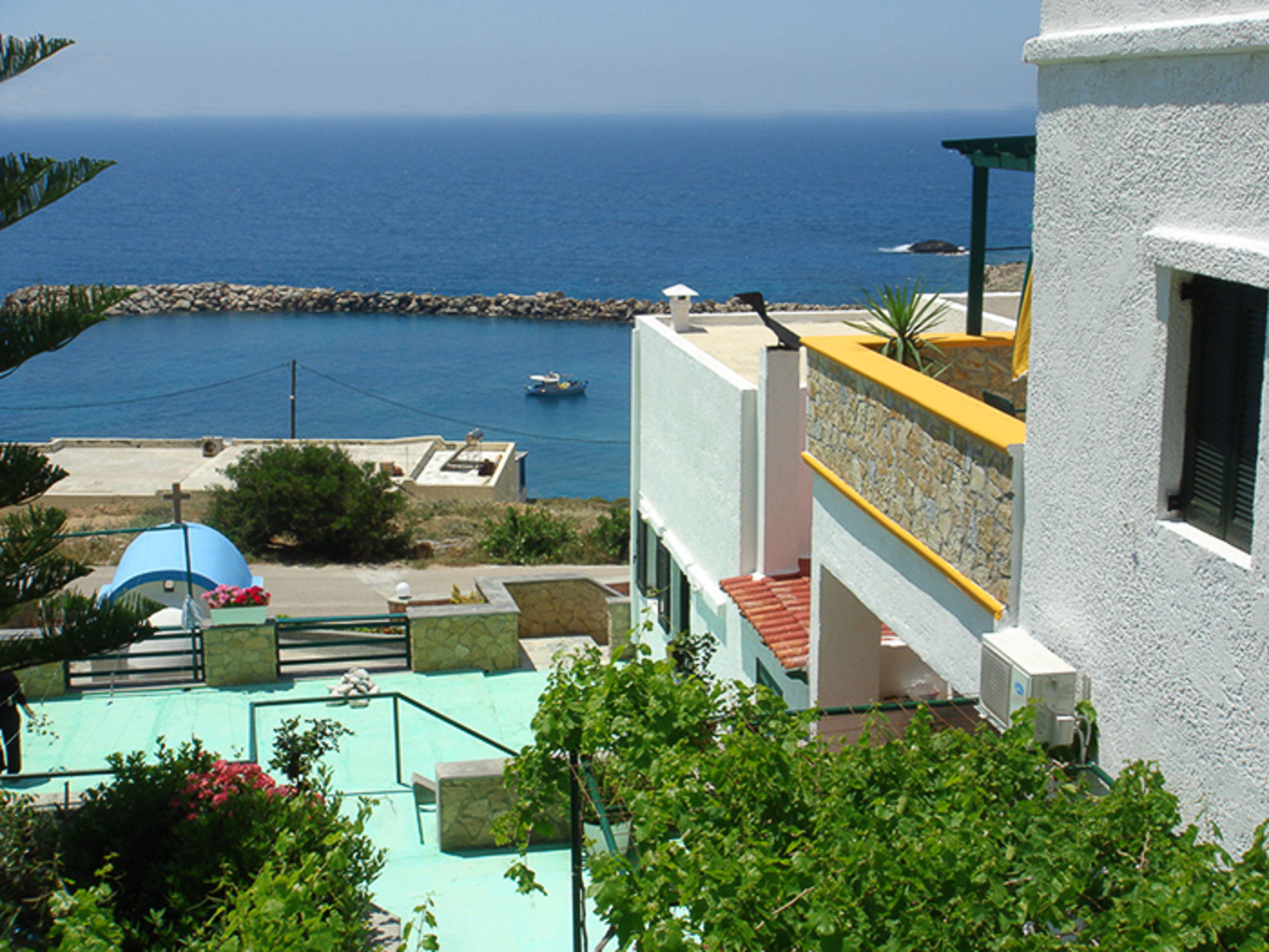 A coastal building with a rooftop pool, a view of the sea, and a small boat in the distance.