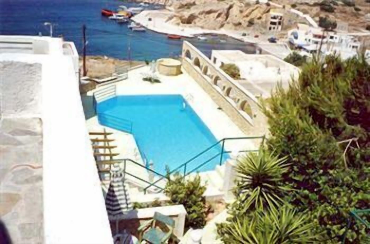 Una piscina con una escalera que baja hacia el agua, rodeada de vegetación y con vistas a la costa, donde se ven barcos y edificios.