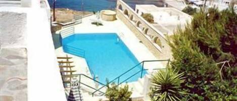 Una piscina con una escalera que baja hacia el agua, rodeada de vegetación y con vistas a la costa, donde se ven barcos y edificios.