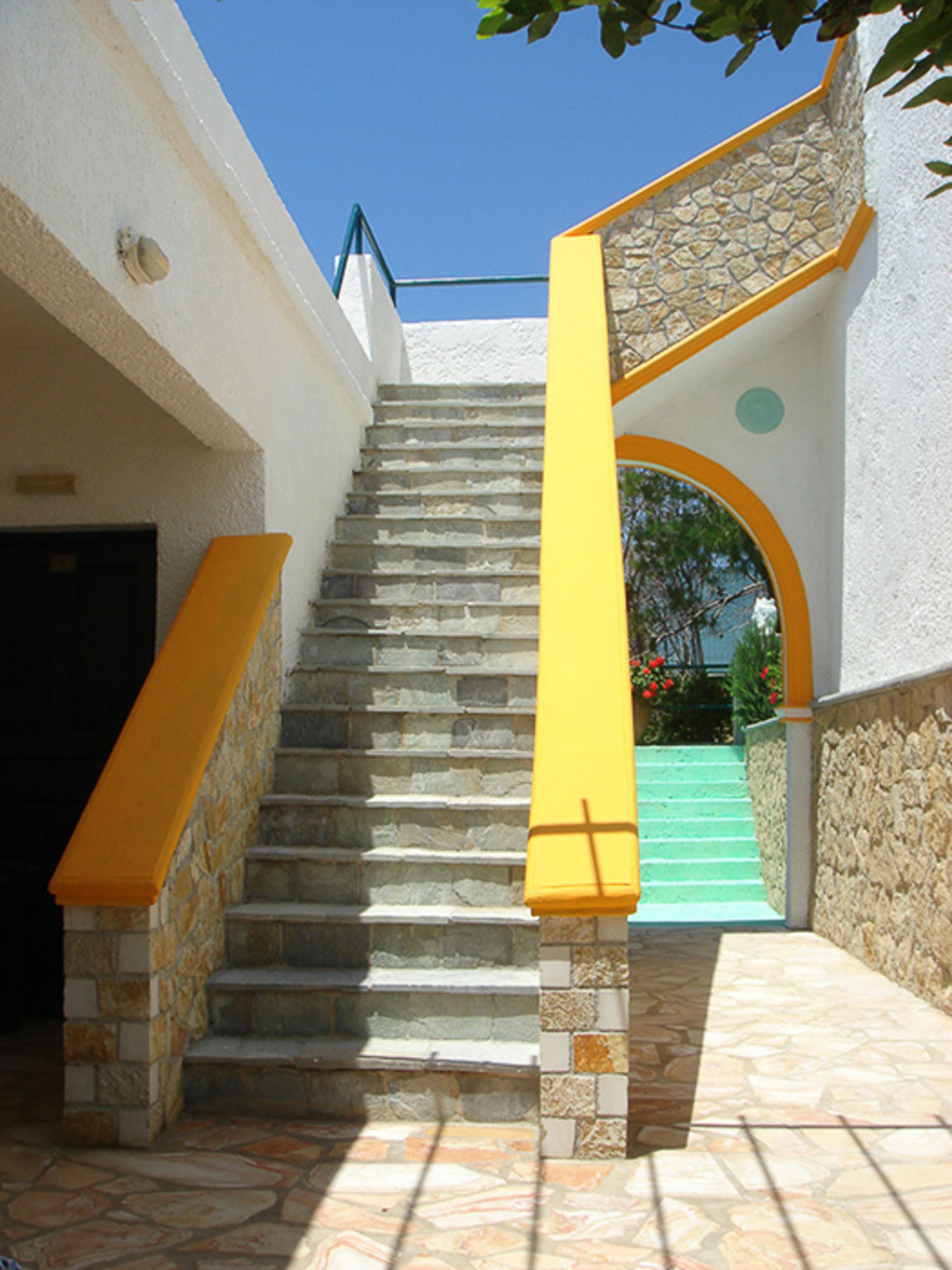 A staircase with stone steps and yellow handrails, leading to a door at the top.