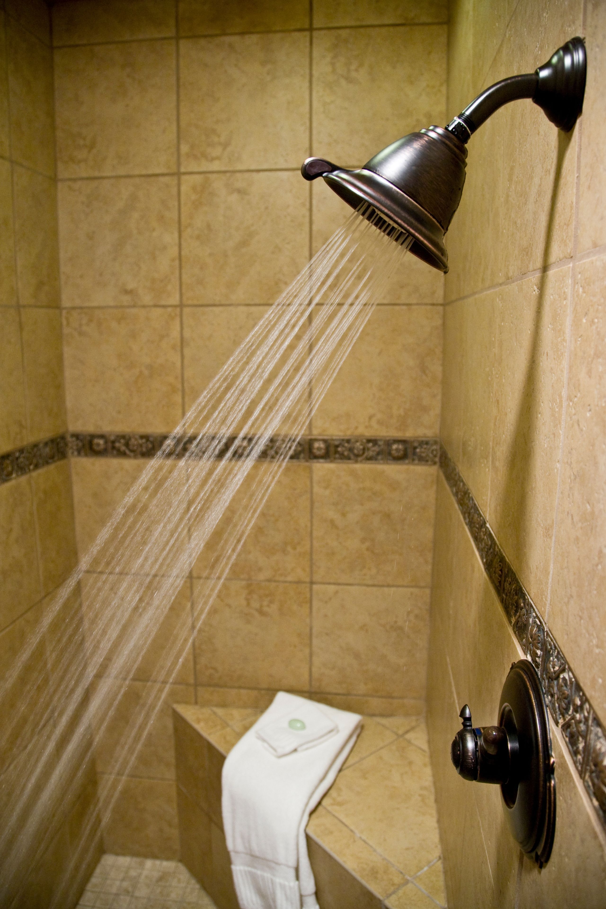 Ducha con cabezal de ducha manual, toallero y una toalla pequeña sobre un banco.