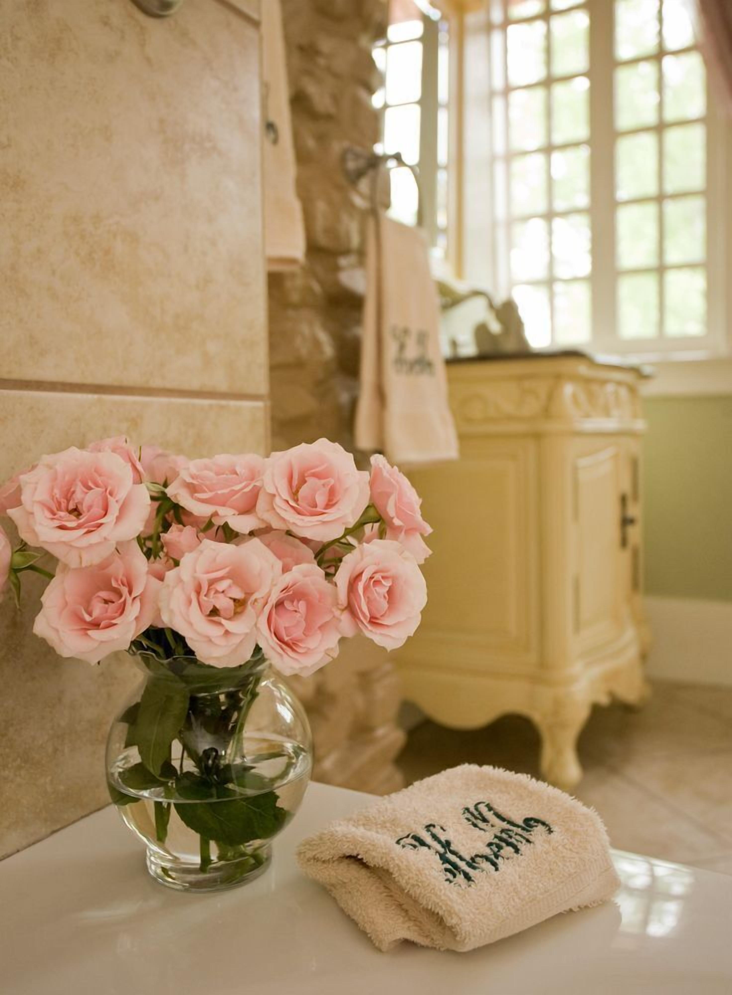 Un baño con un jarrón de rosas rosadas, una toalla y un mueble amarillo.